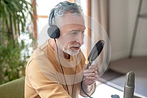 A gray-haired man in black headphones speaking in microphone and looking busy