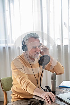 A gray-haired man in black headphones speaking in microphone and looking busy