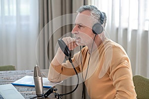 A gray-haired man in black headphones speaking in microphone and looking interetsed