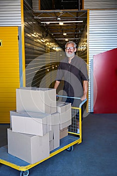 Gray-haired man is carrying lot of boxes on cargo cart