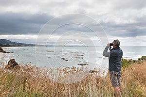 Gray haired man looks in binocular across ocean bay photo