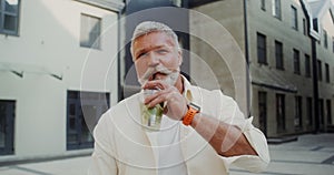 A gray-haired man looks into the camera and drinks lemonade