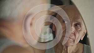 Gray haired man touching wrinkled face with hand looking in mirror