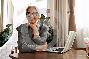 gray-haired mature pretty business woman dressed in a stylish gray jacket sits in a cafe with a laptop