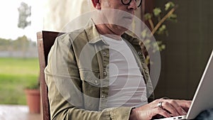 Gray-haired middle aged man using laptop outdoors. Man put feet on table and relax during a break