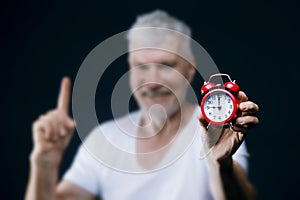 Gray haired senior man with alarm clock in his hands. Sport and health care concept