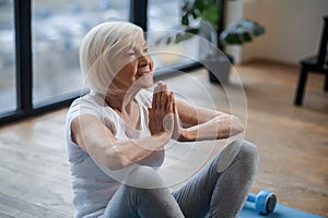 Gray-haired senior woman sitting on the floor and meditating