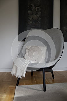 A gray high-backed armchair with black legs, with two paintings behind.\