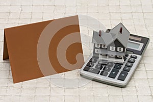 A gray house, brown card and calculator on stone background