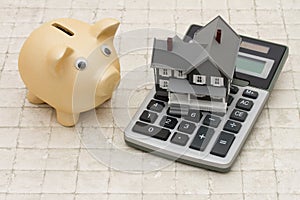 A gray house, piggy bank and calculator on stone background
