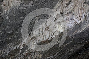 Gray karst cave. Rock formations in the cave, stalactites and stalagmites. Abstract gray grunge background. Stone texture
