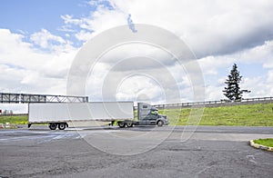 Gray long haul big rig semi truck with dry van semi trailer turning on the local road with hill on the side