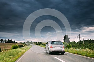 Gray Luxury SUV Car On Country Road At Summer Season. Cloudy Sky Above The Asphalt Motorway, Highway