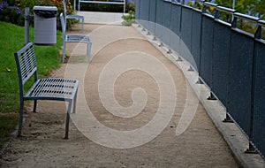 Gray metal benches, railing at the lookout, trash can in the park with a gravel beige path and lawn in summer