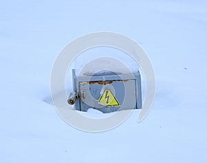 Gray metal electrical panel covered with snow with a high voltage danger sign
