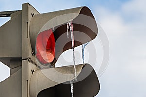 A gray metallic diod traffic light with LED red light on and a group of transparent colored icicles on the blue sky background