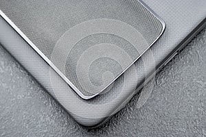 Gray mobile phone with a knitted nylon back lies on a closed textured laptop cover on a gray textural background