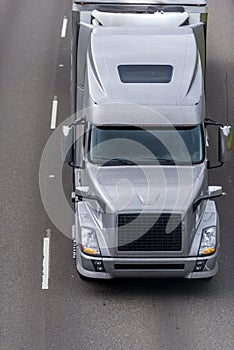 Gray modern big rig semi truck transporting goods in refrigerated semi trailer moving on the wide road