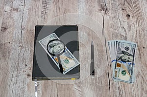 Gray notebook, dollars, magnifier and pen on a wooden table