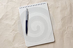 Gray notepad with white coiled spring and pen on a background of beige crumpled craft paper