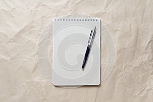 Gray notepad with white coiled spring and pen on a background of beige crumpled craft paper