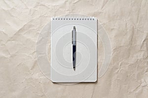 Gray notepad with white coiled spring and pen on a background of beige crumpled craft paper