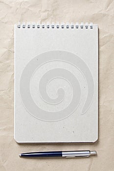 Gray notepad with white coiled spring and pen on a background of beige crumpled craft paper