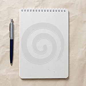 Gray notepad with white coiled spring and pen on a background of beige crumpled craft paper