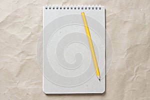 Gray notepad with white coiled spring and pencil on a background of beige crumpled craft paper