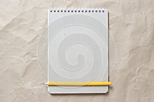 Gray notepad with white coiled spring and pencil on a background of beige crumpled craft paper