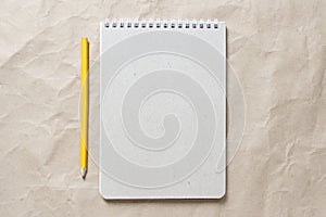 Gray notepad with white coiled spring and pencil on a background of beige crumpled craft paper