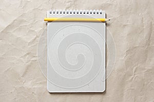 Gray notepad with white coiled spring and pencil on a background of beige crumpled craft paper