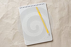 Gray notepad with white coiled spring and pencil on a background of beige crumpled craft paper