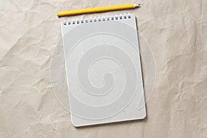 Gray notepad with white coiled spring and pencil on a background of beige crumpled craft paper