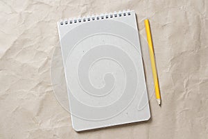 Gray notepad with white coiled spring and pencil on a background of beige crumpled craft paper