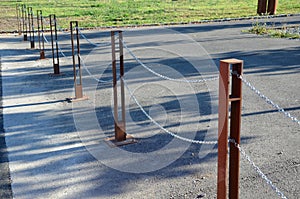 Gray pillars separating the park path from the road. deliberately rusty steel bollards bent into a double space slot connected by