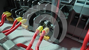 Gray plastic electrical panel with many red wires and yellow bushing ferrules. Close up of a screwdriver is fasten a