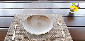 Gray Plate with spoon and fork putting on wooden table for customers to eating food with beautiful flower in glass decorated