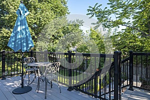 Gray PVC Deck with Black Metal Railing, a Bistro Set and Blue Sun Umbrella in a Backyard