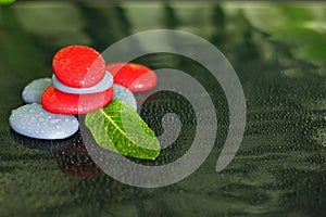Gray and red stones with drops of water and a green leaf arranged in Zen lifestyle on black background