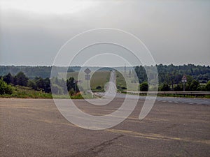 A gray ribbon of road between fields and forests on a cloudy day