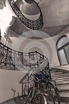 Gray round spiral staircase with black railings with patterns and bicycle view from down