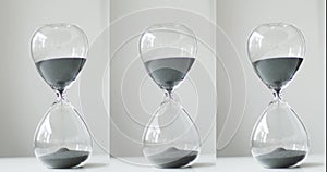 Gray sand running through the hourglass. transparent glass hourglass on the background of a white bedside table