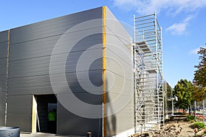 Gray sandwich panel facade of a unfinished warehouse building, tubular multilevel scaffolding