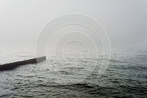 Gray sea in foggy weather and seagulls on the breakwater in the early morning