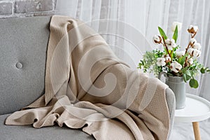 On the gray sofa there is a beige plaid trimmed with lace.