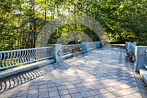 A gray stone bridge over a lake with park benches surrounded by lush green trees and autumn colored trees at Lenox Park