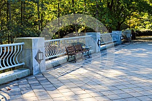 A gray stone bridge over a lake with park benches surrounded by lush green trees and autumn colored trees at Lenox Park