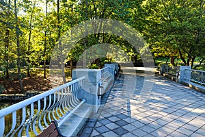 A gray stone bridge over a lake with park benches surrounded by lush green trees and autumn colored trees at Lenox Park