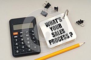 On a gray surface, a calculator, a pencil and a notepad with the inscription - WHAT IS YOUR SALES PROCESS